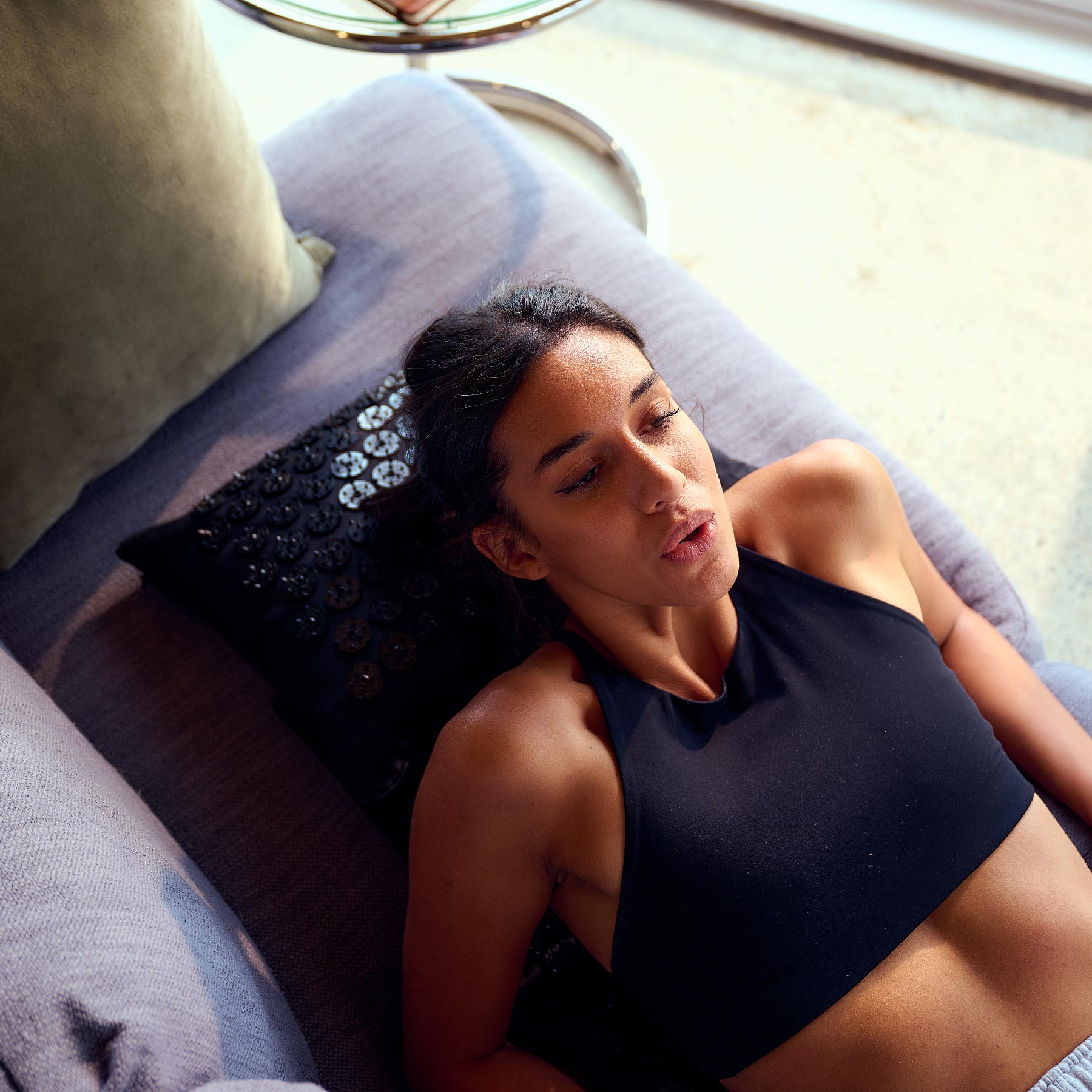 Woman in a black tank top lying on a Shakti Mat and Pillow on a couch